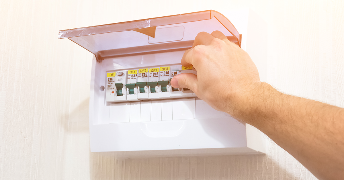 Man uses a flame to see a fuse box near a ceiling with a significant water leak.