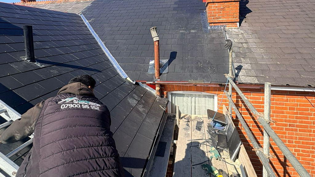 Two professional roofers in safety gear installing clay tiles on a house roof renovation project.