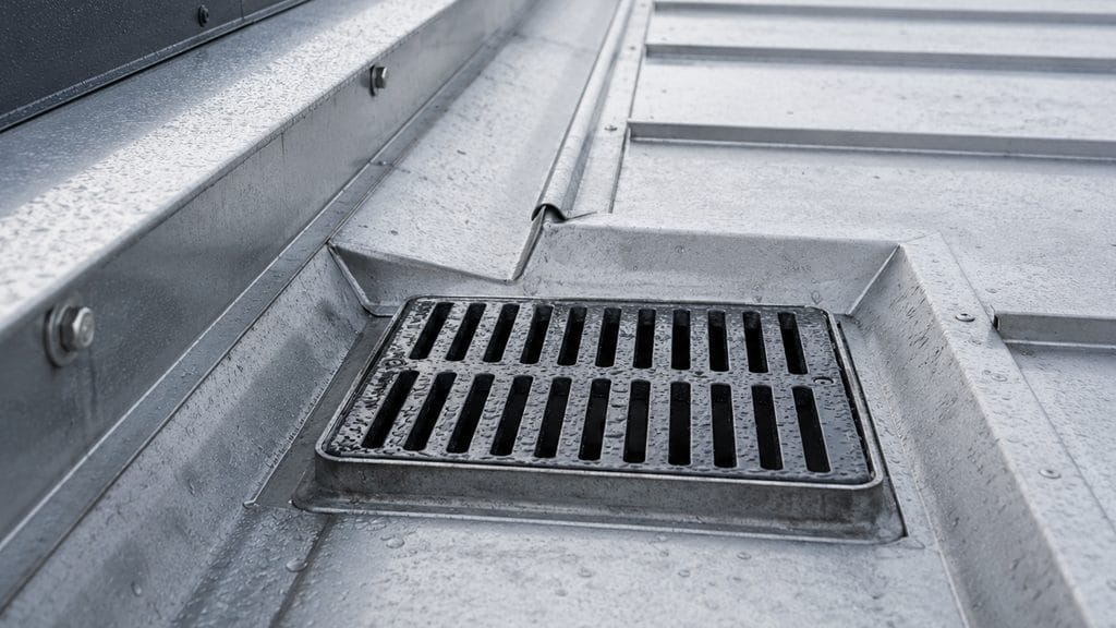 A close-up view of a metal roof drainage system with a grate on a commercial rooftop.
