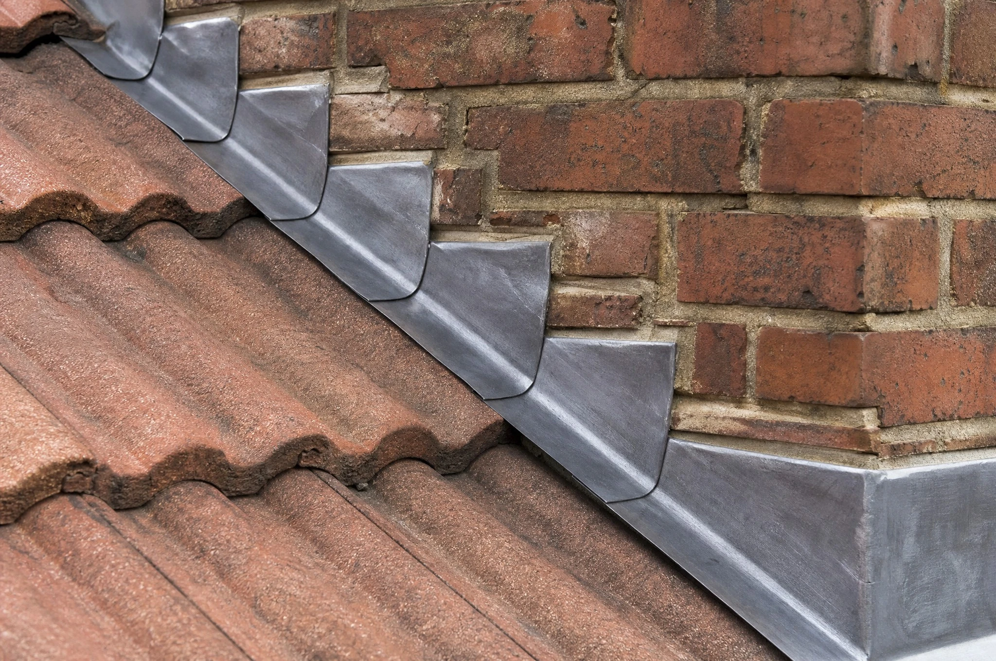 Close-up of stepped lead flashing dressed into brick chimney stack pointing on a UK tiled roof